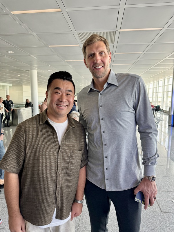 two men standing together in a room with large windows